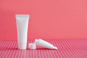 White cosmetic tubes on pink polka dot background. Blank opened plastic container, simple packaging design template. shallow depth of field, copy space photography.