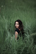 © Serhii - Pretty woman sitting on the grass in dark dress. Beautiful woman posing in tall grass. Brunette lady in field at sunset. Freedom concept background