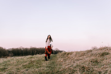 Stylish traveler woman with hat holding map on top of mountains, emotional happy moment, travel concept, space for text. Girl  walking along the grass at the top of the mountain in sunset