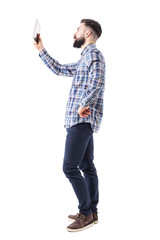 Wall Mural - Side view of bearded young business man holding up pad tablet computer. Full body length portrait isolated on white studio background. 