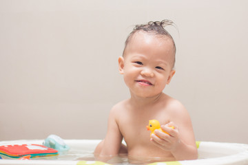 Wall Mural - Cute little Asian 18 months / 1 year old toddler baby boy child taking a bath at home, Smiling kid having fun in bath time playing with yellow rubber duck toys, Hygiene care for young children concept