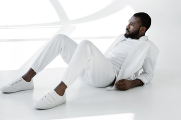 handsome stylish african american man in white clothes lying on white