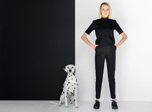 Beautiful Stylish Blonde Woman In Black Clothes Standing Near Black And White Wall With Dalmatian Dog