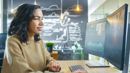 Poster - In the Creative Agency Beautiful Young Woman Videographer Works on Her Personal Computer, Editing Video and Audio Footage. In the Background Her Coworker and Chalkboard with Plans Drawn.