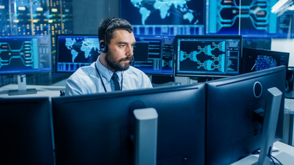 Leinwandbilder - In the System Monitoring Room Dispatcher Wearing Headset Observers Proper Functioning of the Facility. He's Surrounded by Screen Showing Technical Data.