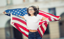 Happy Young American School Girl Holding And Waving In The City With USA Flag