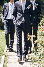 Stylish Groom In Suit Walking With Groomsmen In  Sunny Garden On Wedding Day. Luxury Men In  Rich Outfits Standing Together. Friendship