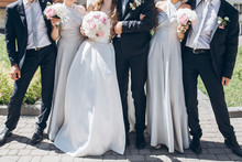 gorgeous bride with peony bouquet and stylish groom posing in sunny garden with bridesmaids and groomsmen on wedding day. luxury wedding couple having fun with friends