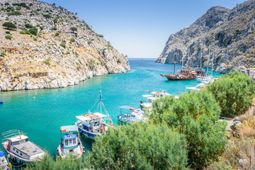 Beautiful sunny coast view to the greek blue sea with crystal clear water beach with big tourist boat cruising around pier in Vathys Bay , Patmos Island, Kos, Dodecanese Islands, Greece