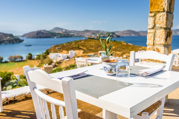 Your table is already reserved at the greek mediterranean sea behind crystal clear blue water and a beautiful coastal aegean bay with fishermen boats cruising, Patmos Island, Kos, Dodecanese, Greece