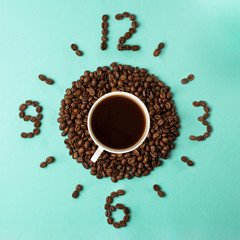 Coffee cup and roasted beans arranged as clock face on blue background, top view. Coffee time symbol. Interesting idea energy and refreshment concept.