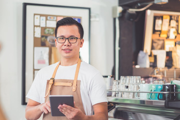 Poster - Asian male barista wear apron hold tablet computer coffee menu with smiling face in cafe waiting order from customer ,Coffee business owner concept