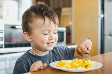 a child in a t-shirt in the kitchen eating an omelet, a fork