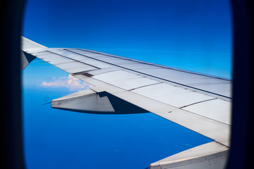 Airplane wing in blue sky, view through plane window. Travel by air. Aircraft window view.