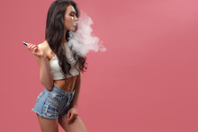 Casual Pretty Woman Standing And Vaping On Pink Background In Studio.