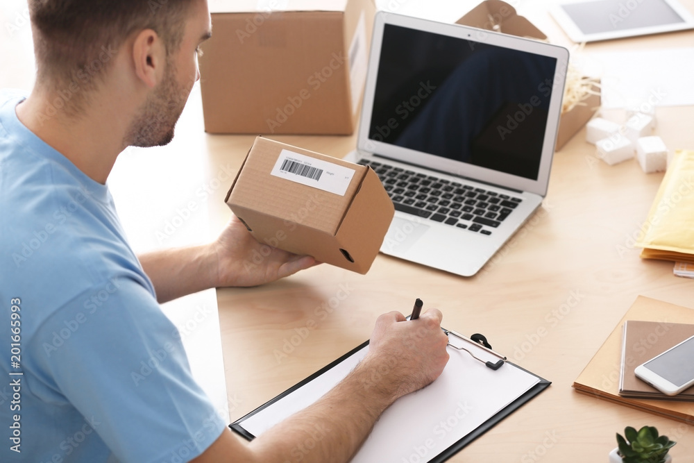 Young man preparing parcel for shipment to client in home office