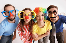 Young Friends In Funny Disguise Posing On Light Background. April Fool's Day Celebration