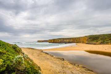 Cloudy sunny summer coast view to a beautiful sandy beach bay and rocky erosion sand limestone cliff of Great Ocean Road, walking at Loch Ard Gorge, Port Campbell National Park, Victoria/ Australia