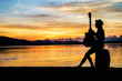 © Anusorn - woman traveler have baggage and guitar sitting and looking for view of lake mountain and sunset near the dam on vacation.silhouette concept.