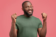 © wayhome.studio  - Portrait of successful dark skinned African American male enterpreneur clenches fists with happiness, celebrates his victory, has broad positive smile on face, isolated over pink background.
