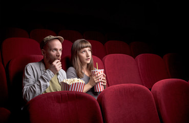 Wall Mural - Young cute couple sitting alone at red movie theatre and having fun