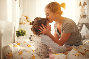 mother wakes her daughter in bed in morning