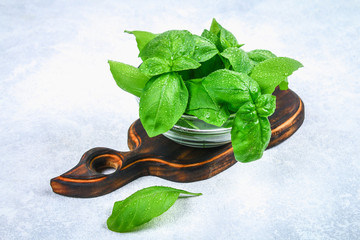 Green fresh homemade basil, spicy herb in a glass bowl on a cutting board on a gray concrete table.