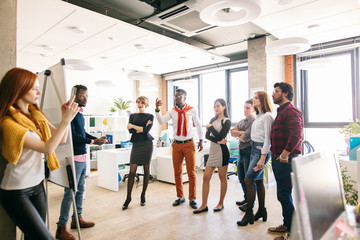 Wall Mural - diverse staff members in casual clothes are standing and looking at afro partner who is presenting his plan on the whiteboard