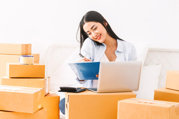 Young woman freelancer working and checklist and writing order with cardboard box on bed at home - SME business online and delivery concept