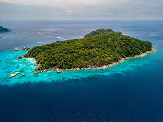 Wall Mural - Aerial view of a deserted, jungle covered tropical island with crystal clear ocean below