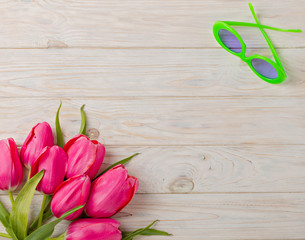 Women's accessories - sunglasses and bouquet of pink tulips on a wooden background.