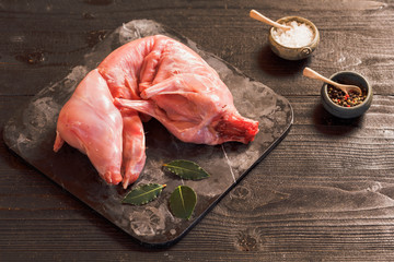 Whole Forest wild rabbit, Raw meat with spices and vegetables, Sea salt, red, white pepper and coriander in clay pots on an old black rustic table, copy space