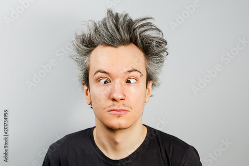 Fotografía Unshorn and unshaven squint young guy with piercings on his face on gray background
