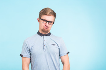 Young funny man wears spectacles isolated over blue background. Bearded wonk looks offended.