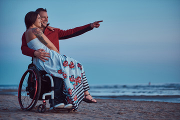 Loving couple, a woman sits on her husband's lap, resting on a beach against a background of a bright dawn.