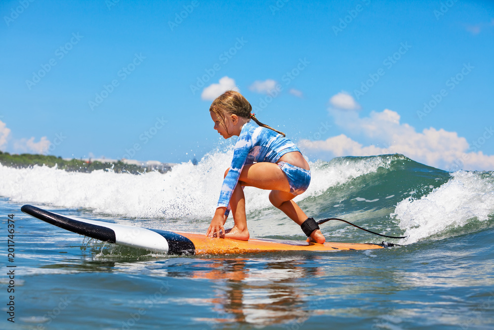 Happy baby girl - young surfer ride on surfboard with fun on sea waves. Active family lifestyle, kids outdoor water sport lessons and swimming activity in surf camp. Summer vacation with child. - obrazy, fototapety, plakaty 