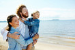 © pressmaster - Happy family of three embracing while enjoying hot summer day on the beach at leisure