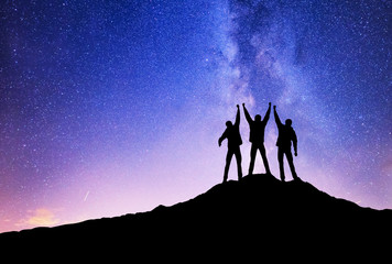 Wall Mural - Silhouettes of team on mountain peak. Sport and active life concept on the night sky background.