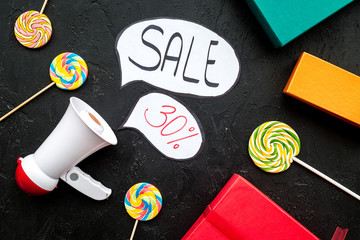 Sale concept with megaphone. Declare the sale. Electronic megaphone near word sale in cloud, gift boxes and sweets on black background top view