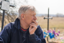 A Gray-haired Village Man A Widower Sadly Sits Near A Fresh Grave And Smokes A Cigarette