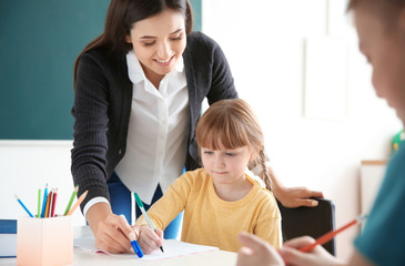 Wall Mural - Female teacher helping girl with her task in classroom at school