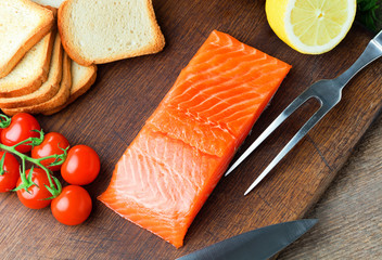 Wall Mural - salmon fillet with tomatoes, lemon and bread on wooden background