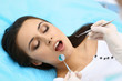 © rogerphoto - Young female patient visiting dentist office.Beautiful woman with healthy straight white teeth sitting at dental chair with open mouth during oral checkup while doctor working at teeth