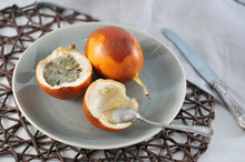 Granadilla Is An Exotic Tropical Fruit. Two Fruits Lie On A Plate. One Of The Fruits Is Cut In Half. In The Frame Cutlery. Close-up.