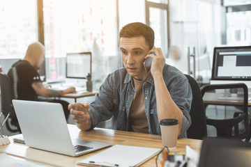 Poster - Portrait of concentrated male telling by phone while pointing at laptop. He working in office. Professional conversation concept