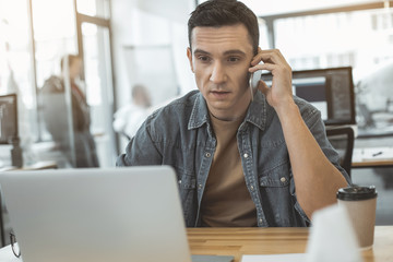 Poster - Portrait of serene man talking by mobile while typing in notebook computer at desk. Serious employer at job concept