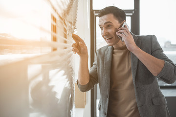 Poster - Portrait of cheerful businessman talking by mobile while looking at window. Happy worker during conversation at job concept