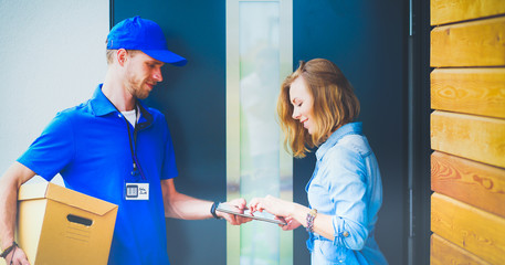 Smiling delivery man in blue uniform delivering parcel box to recipient - courier service concept. Smiling delivery man in blue uniform