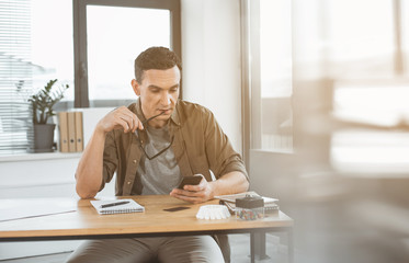 Poster - Portrait of thoughtful worker typing in mobile while situating at desk. Wistful employer during job concept. Copy space