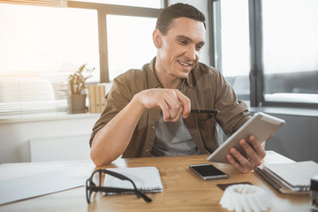 Poster - Portrait of happy businessman looking at electronic tablet while sitting at desk in office. Cheerful employer during labor with technology concept